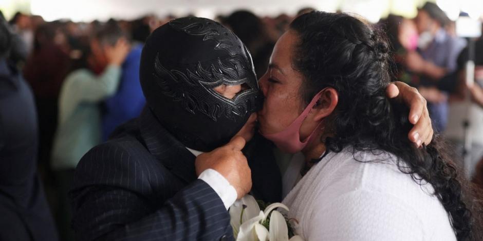 Un luchador, quien porta una máscara negra, besa a su ahora esposa tras casarse en una boda masiva en Neza.