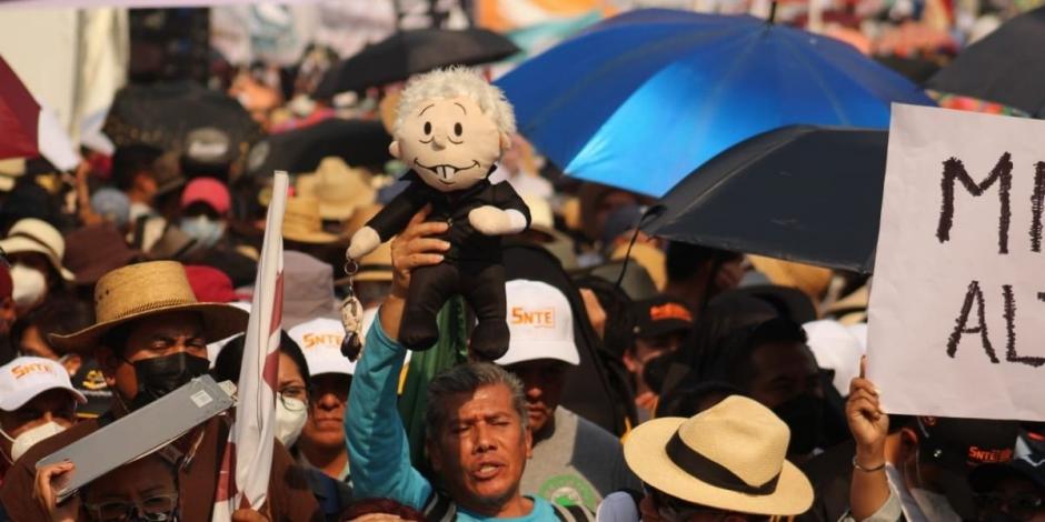 Un muñeco de AMLO sobresale de entre la multitud, en medio de sombrillas y carteles en apoyo al mandatario federal.