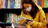 Una mujer que usa cubreboca y guantes revisa dos libros en una librería.