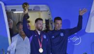 El futbolista argentino Lionel Messi sostiene el trofeo del Mundial de la FIFA a la salida de un avión junto al técnico Lionel Scaloni, en Buenos Aires, Argentina, el martes 20 de diciembre 2022