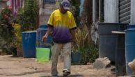 Un hombre camina por la calle cargando cubetas con agua.