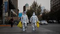 Trabajadores de prevención con trajes protectores cruzan una calle mientras continúan los brotes de la enfermedad por COVID-19.