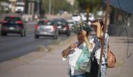 Un par de mujeres en la calle cubren sus ojos del sol, una de ellas lo hace con la mano y la otra con un abanico
