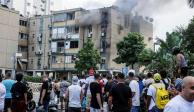 Varias personas se reúnen mientras sale humo de un edificio de apartamentos residenciales después de que un cohete, disparado desde la Franja de Gaza hacia Israel, cayera en Tel Aviv, Israel, 27 de octubre de 2023.