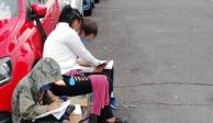 La mujer ayuda y sus dos hijos estudiando en la calle.