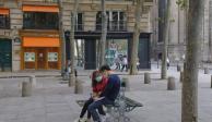 Una pareja con mascarillas sentada en el banco de una plaza.