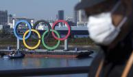 Un hombre con cubrebocas pasa frente a los anillos olímpicos en Tokio el e de diciembre de 2020.