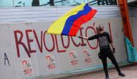 Un hombre ondea la bandera colombiana frente a un grafiti que dice "Revolución" durante una protesta que exige medidas gubernamentales para abordar la pobreza, la violencia policial y las desigualdades en los sistemas de salud y educación, en Bogotá, Colombia