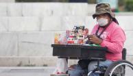 Una mujer en silla de ruedas vende cigarros y golosinas. Utiliza un cubrebocas para protegerse del COVID-19