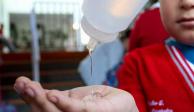 A un niño con uniforme escolar le ponen gel antibacterial en la mano para protegerse del coronavirus