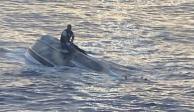 Un hombre, que dice ser una de las 40 personas que abandonaron Bimini, Bahamas, el sábado antes de encontrarse con un clima severo, se sienta en un bote volcado frente a las costas de Florida.
