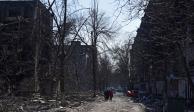 Residentes locales que aún quedan en la ciudad, recorren una calle dañada por el ejército ruso, en la sitiada de Mariupol, ayer.