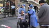En China, expertos de salud ayudaron a un hombre en silla de ruedas durante las pruebas masivas COVID-19.