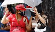 Dos mujeres se protegen del sol con un paraguas, y del COVID-19 con cubrebocas