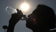 A contra luz, un hombre toma agua de una botella para mitigar el calor