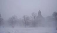 Un peatón con equipo para la nieve avanza por el Colonial Circle, con la silueta de la iglesia episcopaliana de St. John's Grace entre la ventisca, en Buffalo, Nueva York, el sábado 24 de diciembre de 2022