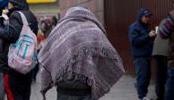 Una persona camina por la calle con una cobija a cuestas para protegerse de las bajas temperaturas