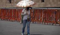 Tercera ola de calor continúa en México; en foto, una mujer se cubre del sol mientras camina por el Zócalo de la Ciudad de México.
