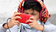 Un niño con audífonos se entretiene con un videojuego en un celular