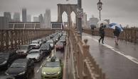Personas con sombrillas caminan a un costado de los vehículos por el Puente de Brooklyn, luego de las fuertes lluvias del viernes 29 de septiembre de 2023, en Nueva York.