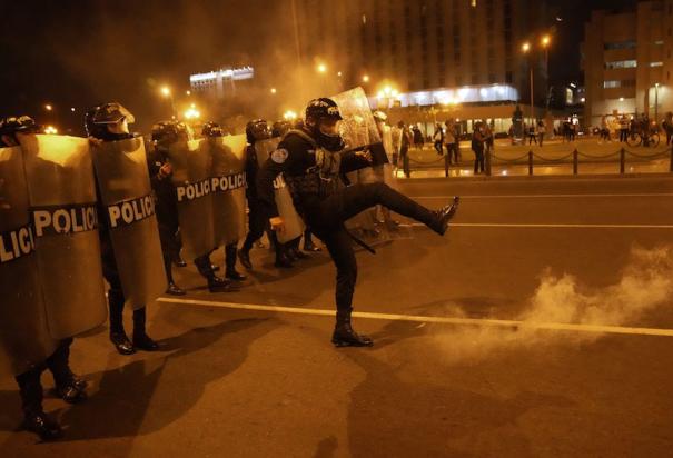 Un oficial en plena formación patea una bomba lacrimógeno devuelta por manifestantes.