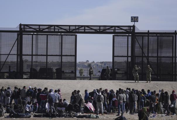 Migrantes que cruzaron la frontera desde México hacia Estados Unidos esperan a un costado del muro fronterizo en donde agentes de la Patrulla Fronteriza de Estados Unidos montan guardia, el 30 de marzo de 2023, en una imagen tomada desde Cuidad Juárez, México.