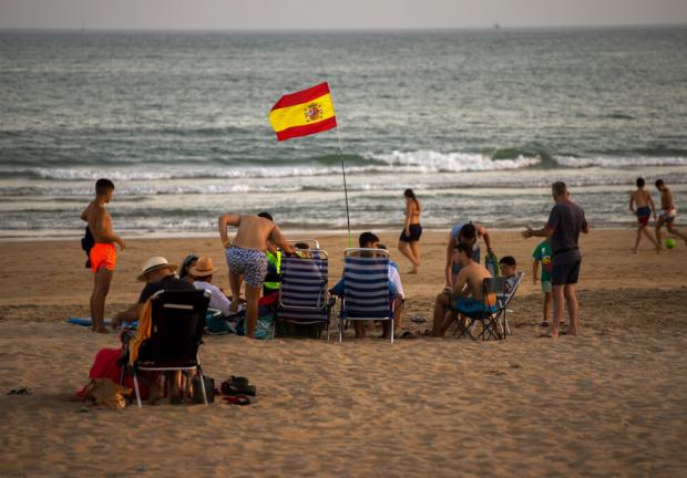 Una bandera española ondea mientras los bañistas disfrutan de un día de playa en Barbate, en la provincia de Cádiz, España, el sábado 25 de julio de 2020.