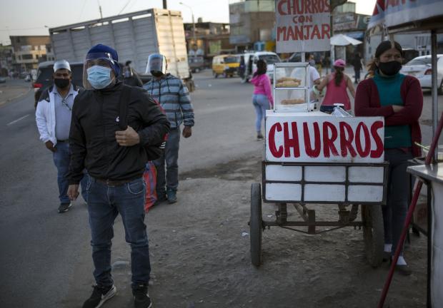 Con mascarillas para frenar la propagación del nuevo coronavirus, los viajeros esperan autobuses públicos en Comas, en las afueras de Lima, Perú.