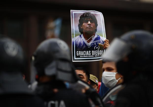 Un hombre sostiene un póster con la cara de Diego Maradona mientras espera en el exterior de la Casa Rosada para acceder a la capilla ardiente, en Buenos Aires, Argentina, el 26 de noviembre de 2020.