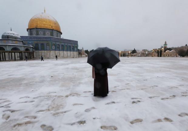 Una mujer junto a la Cúpula de la Roca en el complejo conocido por los judíos como el Monte del Templo y por los musulmanes como el Noble Santuario durante una mañana nevada en la Ciudad Vieja de Jerusalén.