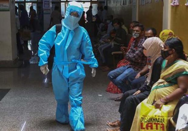 Una mujer india con traje de protección personal camina hacia una sala de COVID-19 de un hospital mientras otros esperan los resultados de sus pruebas en Hyderabad, India