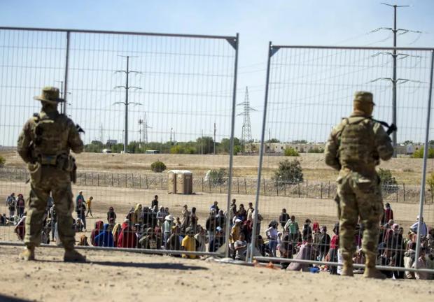 Migrantes esperan junto a una valla fronteriza mientras son vigilados por miembros de la Guardia Nacional de Texas, para ingresar a El Paso, Texas, el miércoles 10 de mayo de 2023.