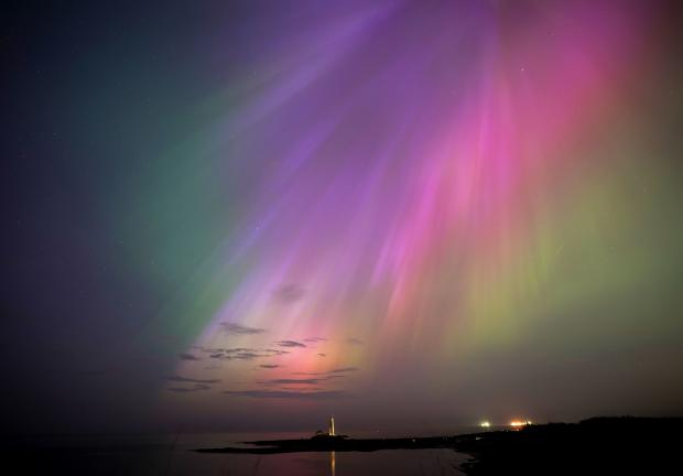 Una aurora boreal brilla en el horizonte en el faro de St. Mary en Whitley Bay, en la costa noreste, Inglaterra, el viernes 10 de mayo de 2024.