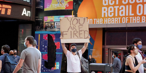 Una persona sostiene un cartel con la leyenda “Estás despedido”, dirigido a Trump.