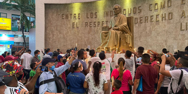 Migrantes orando frente a estatua de Benito Juárez.