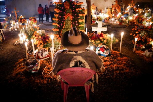 Un hombre sentado frente a una ofrenda de Día de Muertos en Pátzcuaro, Michoacán.