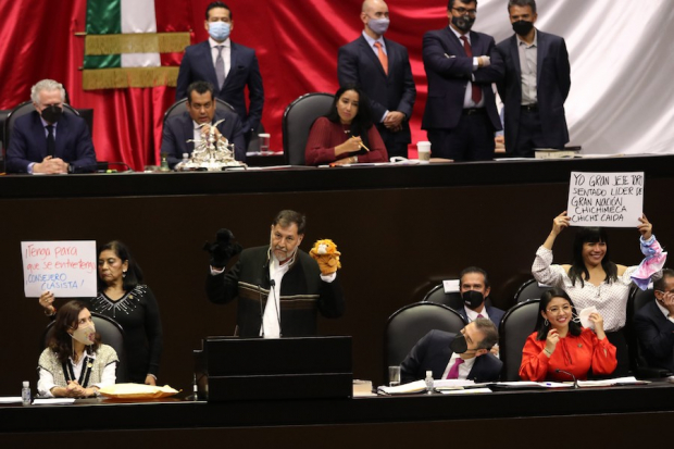 El petista Fernández Noroña muestra dos marionetas durante la comparecencia de Lorenzo Córdova (a su izq.), mientras diputados de la 4T muestran cartulinas con consignas, ayer, en el pleno.