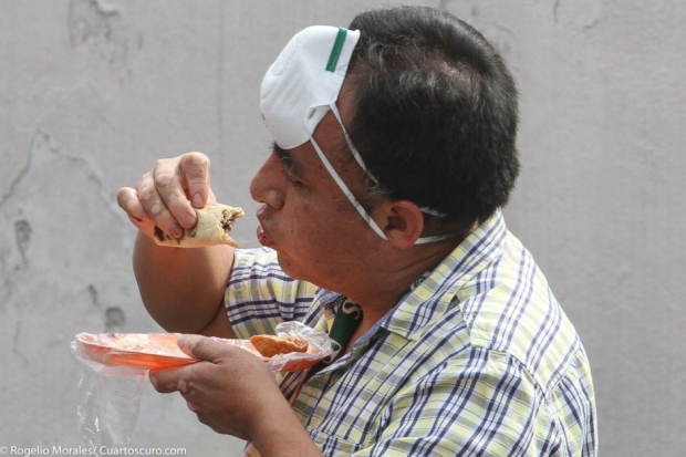 Hombre se coloca el cubrebocas en la frente para poder comer sus tacos.