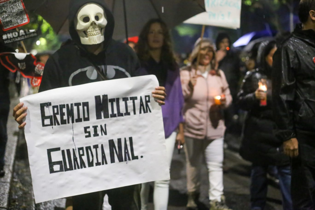 Persona enmascarada con una cartulina con el texto "Gremio Militar sin Guardia Nacional".
