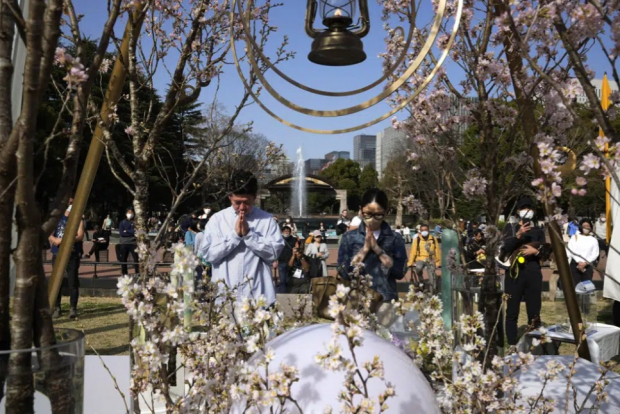 Un hombre y una mujer rezan tras depositar flores en un monumento para conmemorar el 12mo aniversario de un masivo sismo, tsunami y un desastre nuclear, en el Parque Hibiya, en Tokio.