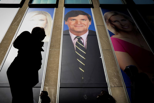 Ciudadanos de EU pasan frente a un promocional de Tucker Carlson en el News Corp. Building de Nueva York.