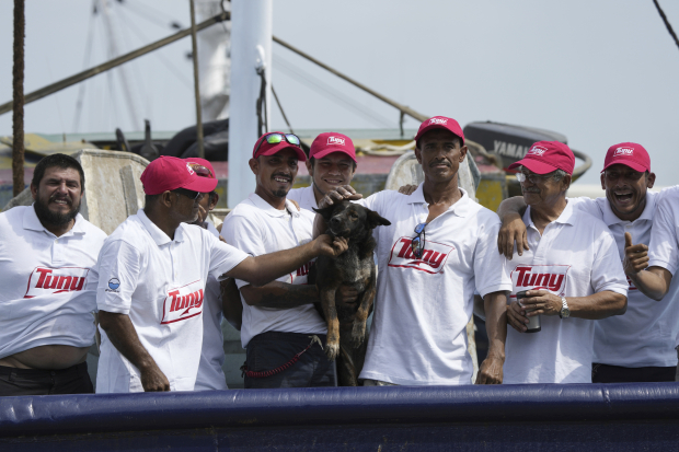 La tripulación del atunero mexicano María Delia posa para las fotos con Bella, la perra del australiano Timothy Lyndsay Shaddock, ambos rescatados de un catamarán dañado en el Océano Pacífico, a su llegada al puerto de Manzanillo, México, el martes 18 de julio de 2023.