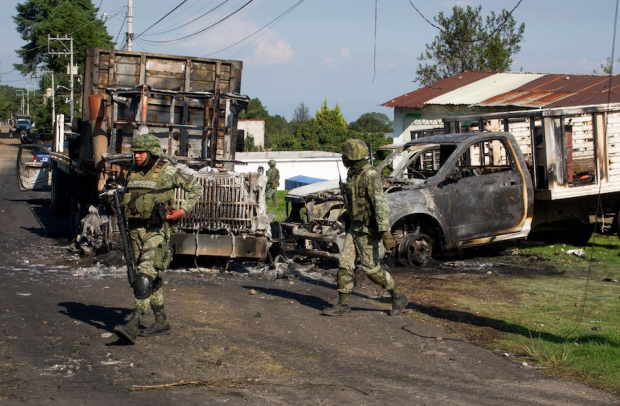Elementos del Ejército caminan junto a dos de los vehículos que fueron quemados en Huitzilac, ayer.