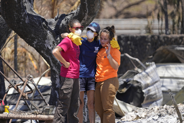 Tres mujeres se abrazan tras rebuscar entre los escombros de una vivienda destrozada por un incendio, el 11 de agosto de 2023, en Lahaina, Hawái