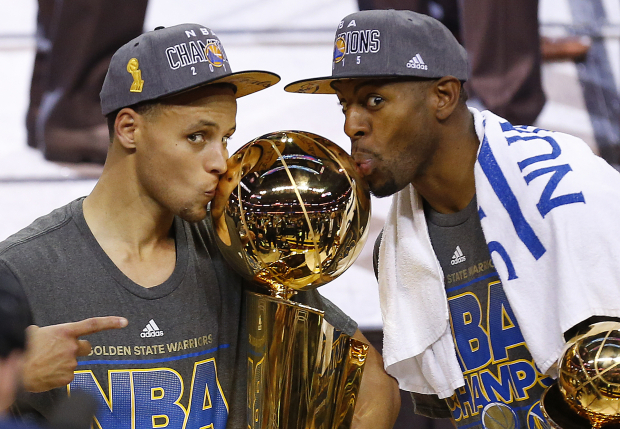 Stephen Curry, izquierda, y Andre Iguodala, de los Warriors besan el trofeo Larry O'Brien después de derrotar a los Cavaliers en el Juego 6 de las Finales de la NBA eN 2015.