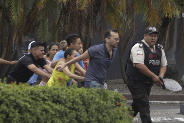 Un policía armado evacúa al personal de la estación del canal de televisión TC después de que un grupo de hombres armados irrumpiera en su set durante una transmisión en vivo, en Guayaquil, Ecuador, ayer, en medio de una jornada marcada por la violencia.