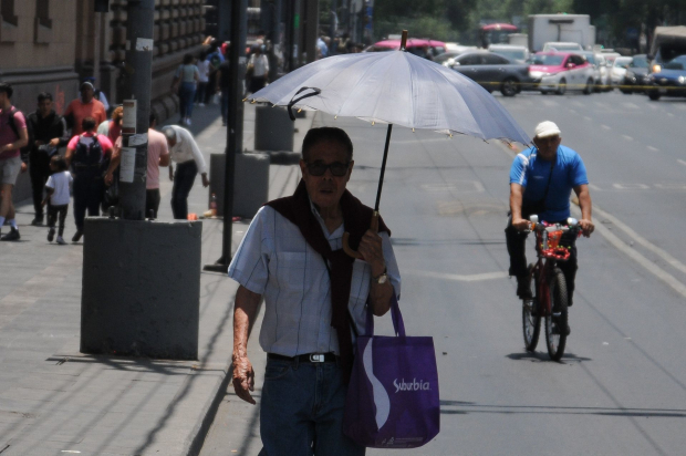 Una persona camina utilizando una sombrilla para protegerse de los rayos del sol.