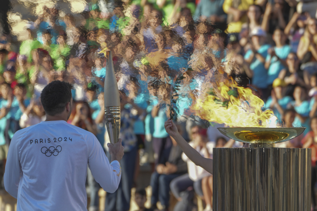 El medallista olímpico griego Ioannis Fountoulis sostiene una antorcha al recibir un ramo de olivo tras encender la llama de los Juegos Olímpicos