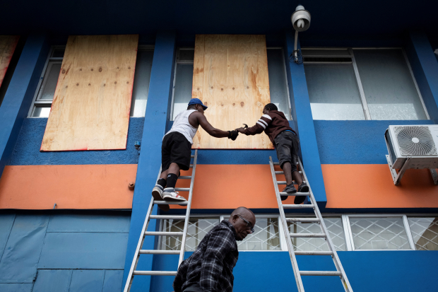 Trabajadores de Jamaica protegen ventanales en edificios de gobierno y puntos críticos.