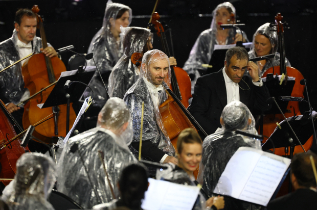 Miembros de la Orquesta Nacional de Francia se protegen de la lluvia en la ceremonia de apertura.
